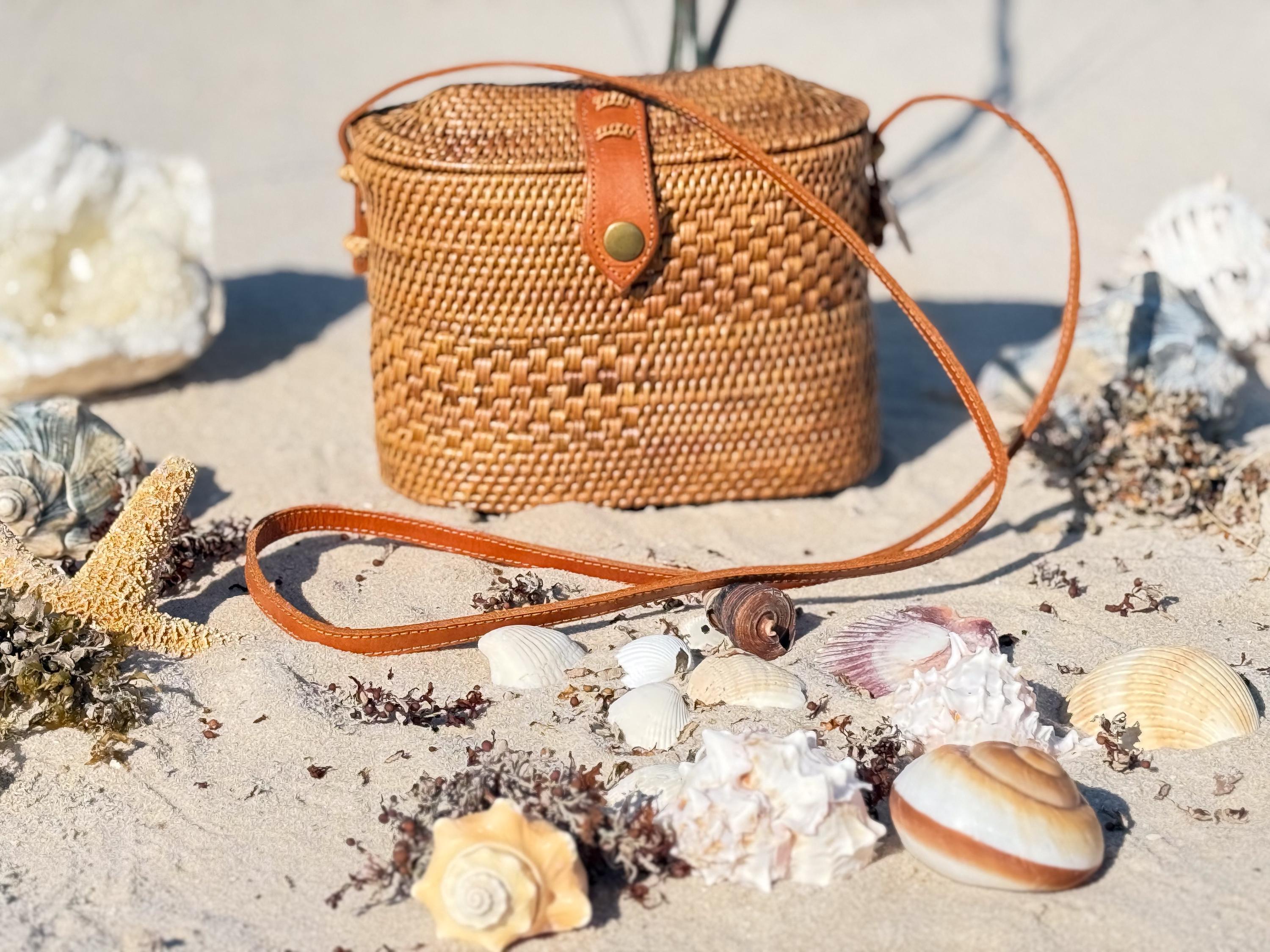 A woven purse sits on a sandy beach, surrounded by various seashells and starfish.
