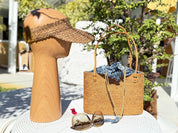 a wooden headpiece, a woven straw bag, sunglasses, and a hat placed on a white table.
