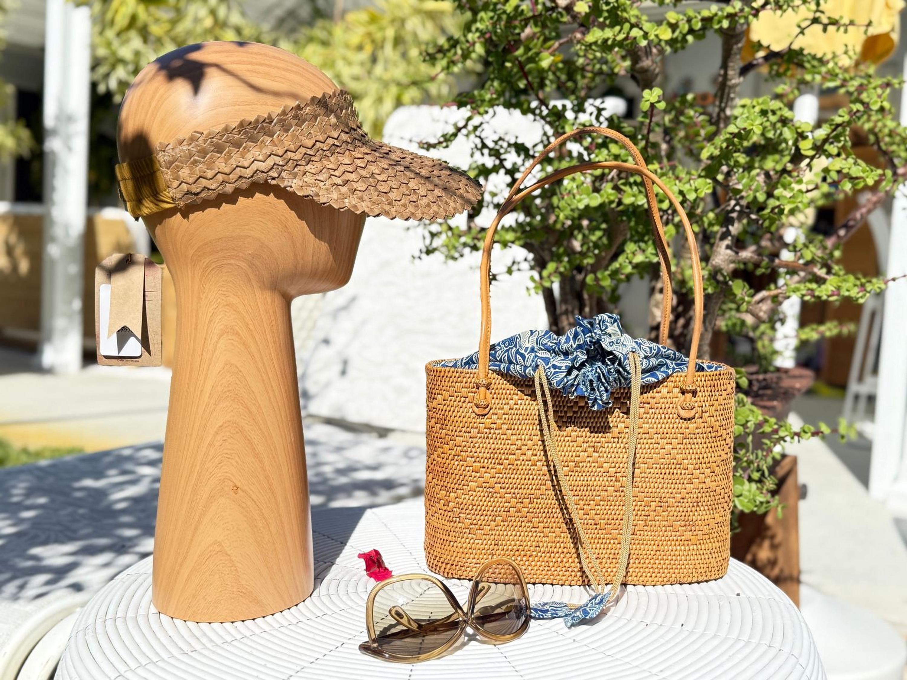 a wooden headpiece, a woven straw bag, sunglasses, and a hat placed on a white table.