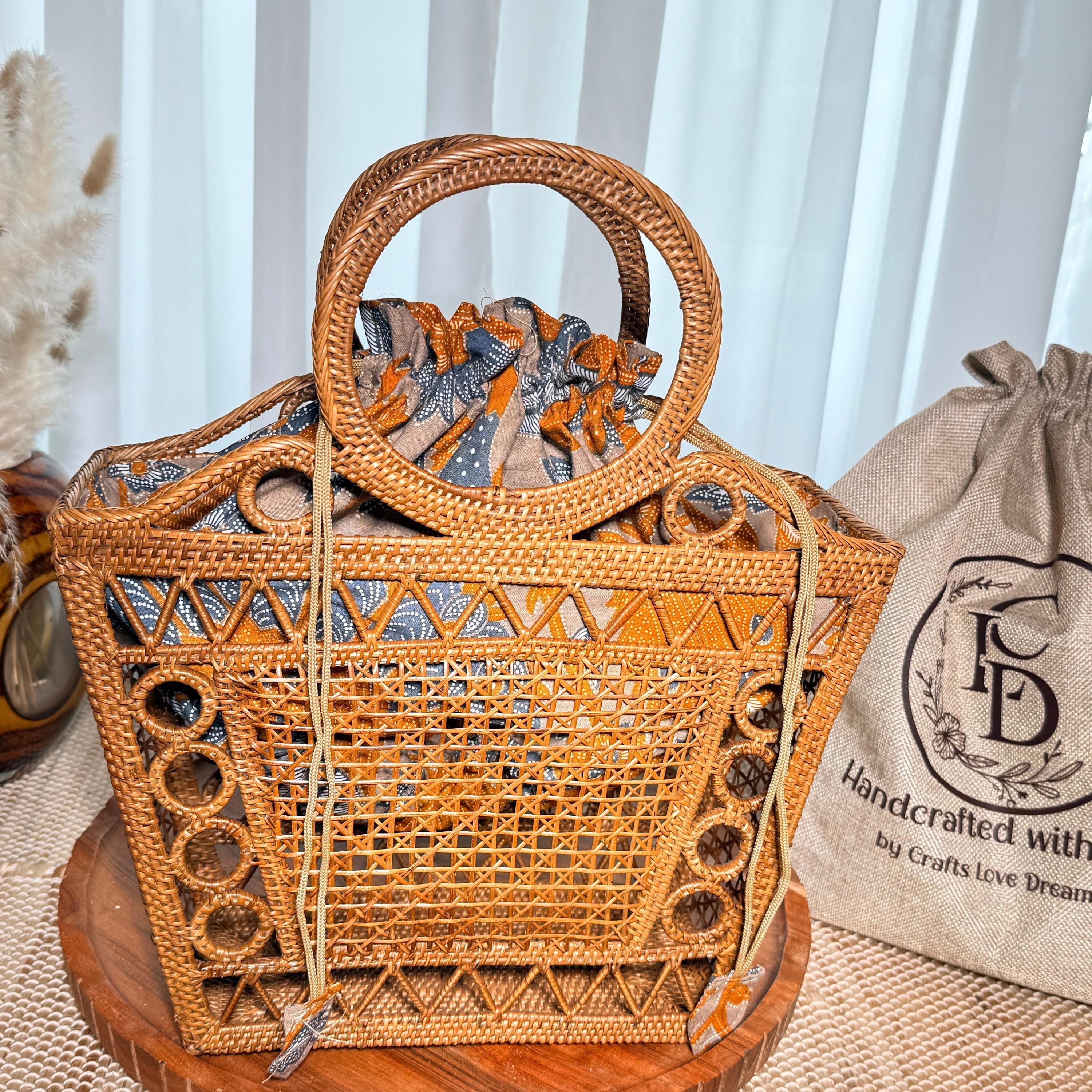 A woven handbag with a round handle and a drawstring closure sits on a wooden surface, accompanied by a burlap sack with the text "Handcrafted with love dream" printed on it.