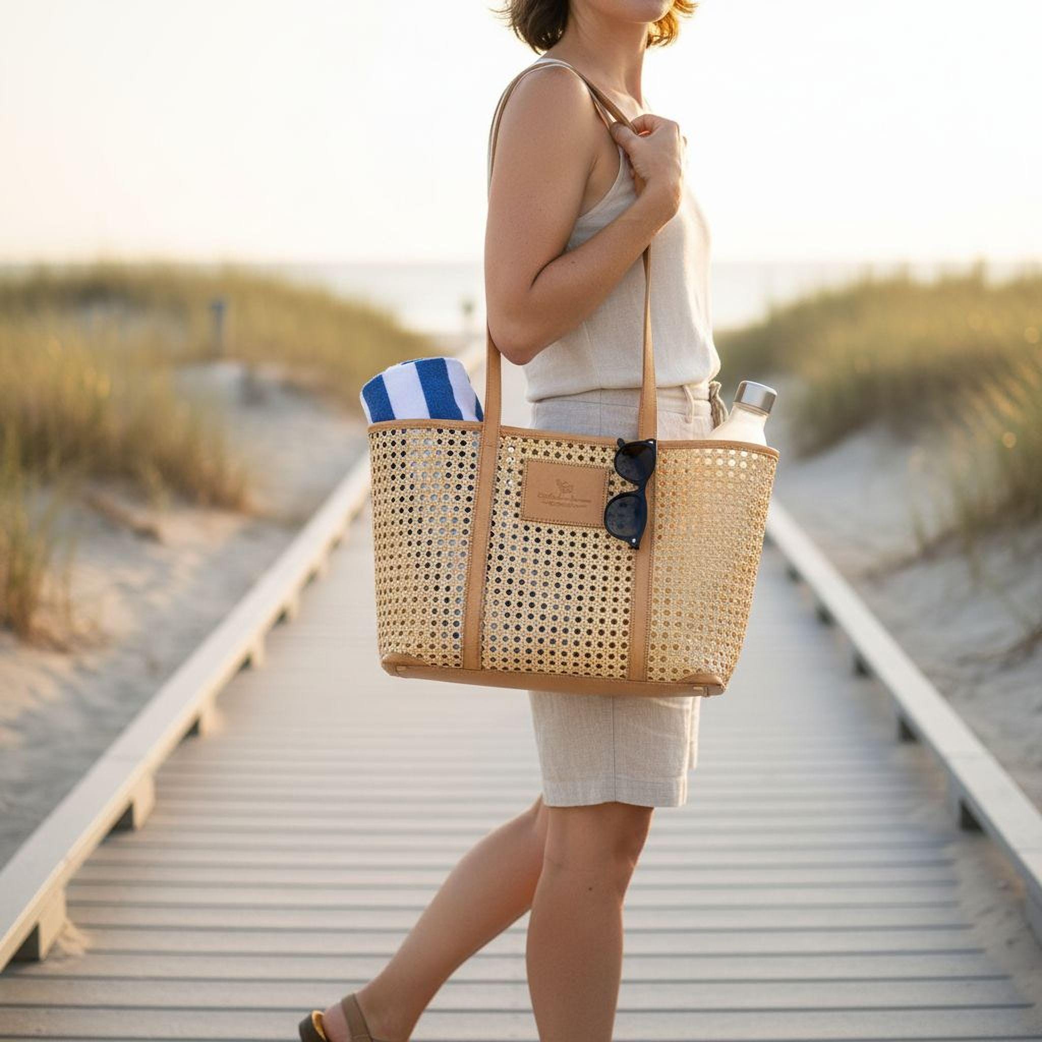 A woman is walking on a wooden boardwalk, carrying a large woven tote bag with a blue and white striped towel inside.