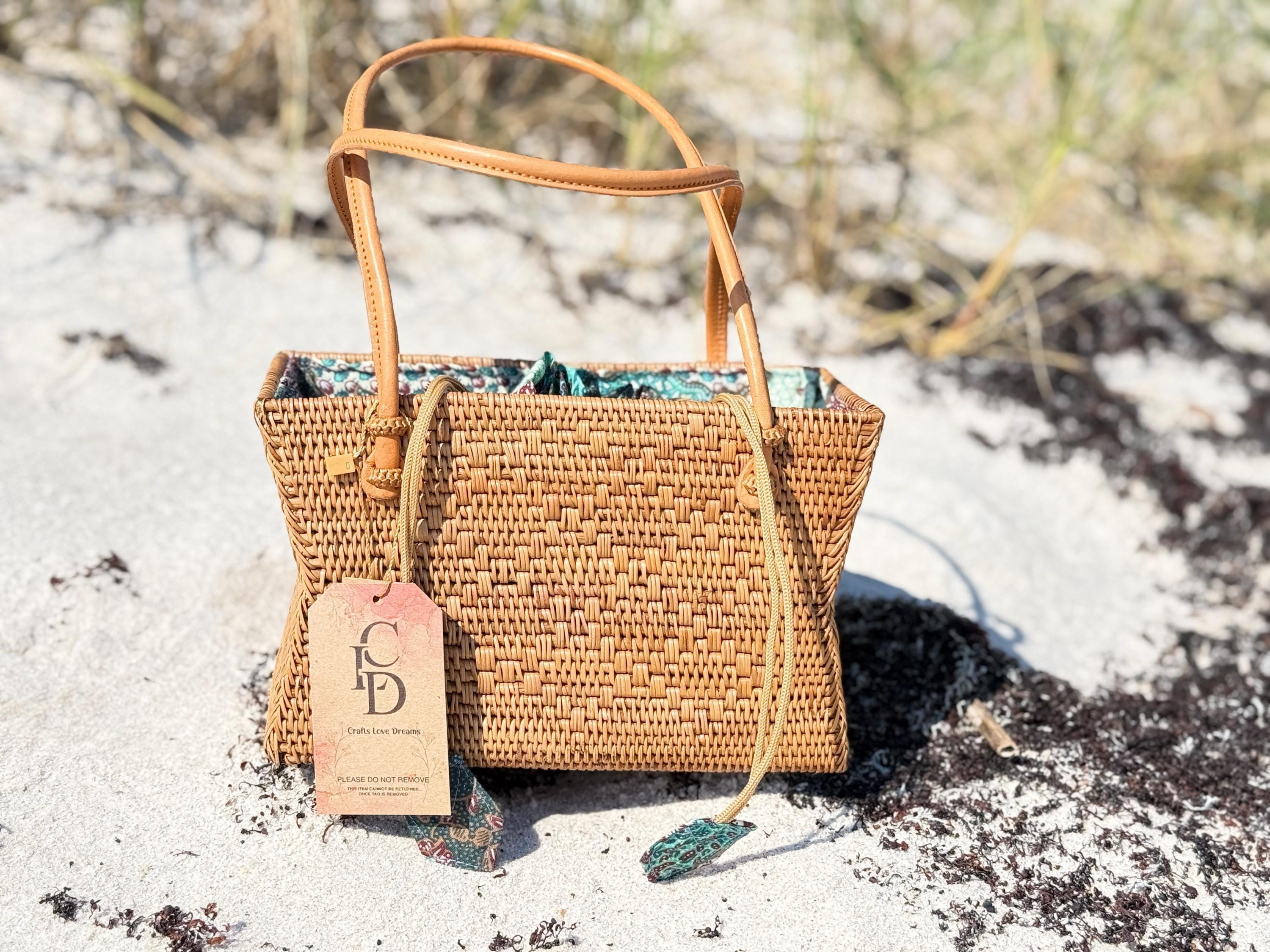 A woven straw handbag with a tag attached, placed on a sandy beach.