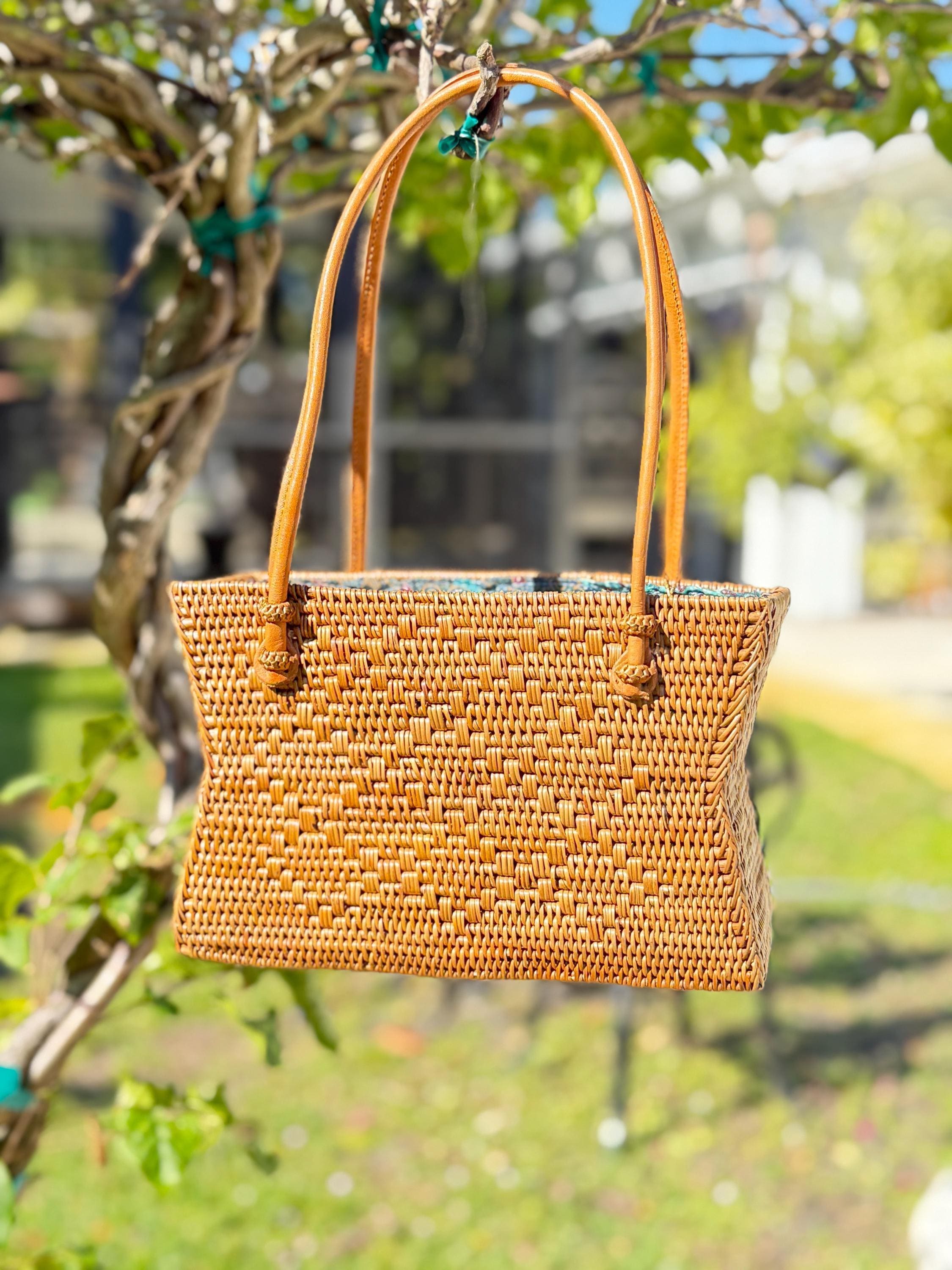 A woven straw handbag is hanging from a tree branch in a garden setting.
