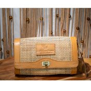 A tan woven purse with a metal clasp and a small label on the front, placed on a wooden surface against a background of wooden strings and beads.