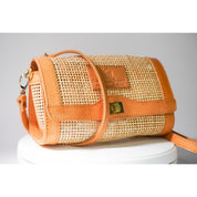 A handbag with a woven texture and a leather strap, sitting on a white surface.