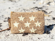 A woven pouch with white star-shaped embellishments sits on a sandy beach.