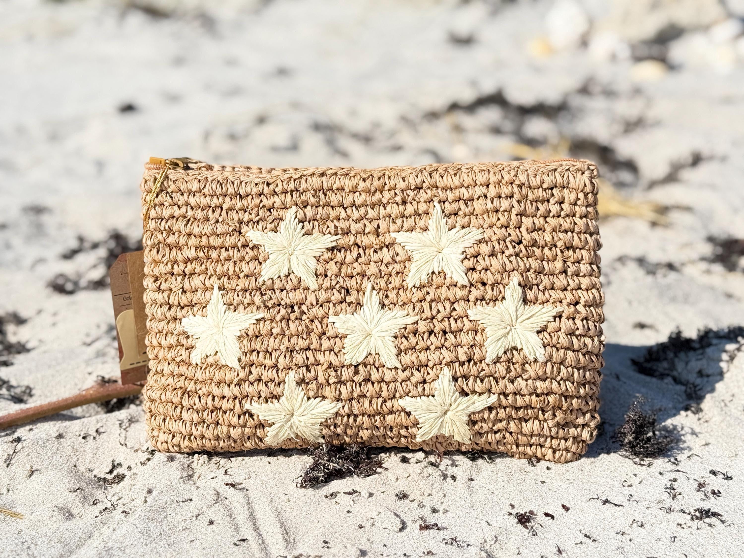 A woven pouch with white star-shaped embellishments sits on a sandy beach.