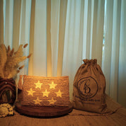 a wooden table with a woven bag, a vase with dried flowers, and a wooden tray with a star-patterned bag.