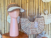 a mannequin head wearing a brown and white woven hat, and a woven handbag with a tag attached, both displayed against a bamboo wall.