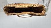 A woven straw bag with a curved handle, sitting on a white surface.