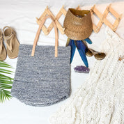 A handbag, a pair of sunglasses, a white lace garment, and a woven hat are arranged on a white surface, along with some natural elements like a green leaf.