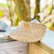 A straw hat with a woven pattern rests on a wooden surface, with a blurred natural background.