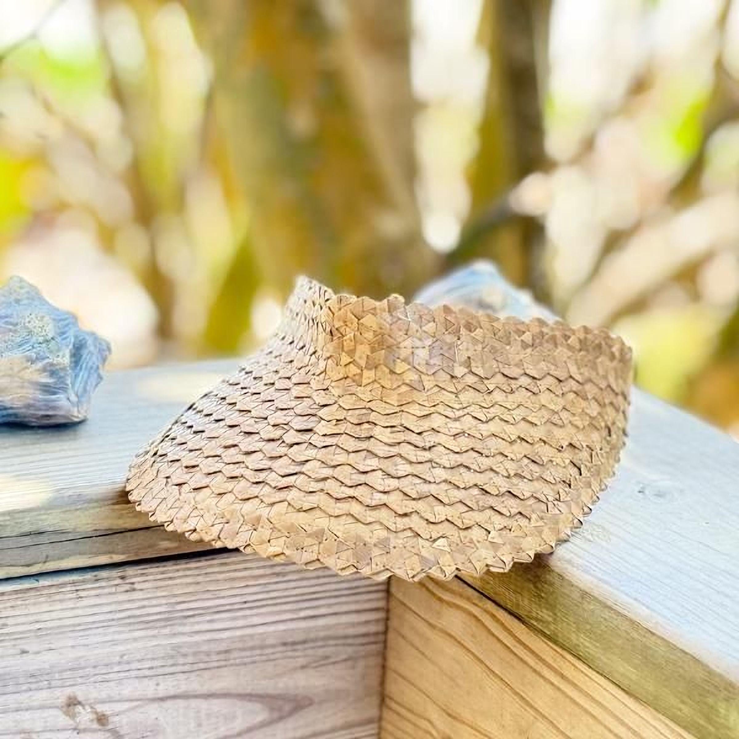 A straw hat with a woven pattern rests on a wooden surface, with a blurred natural background.
