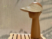 A wooden mannequin head wearing a beige sun visor stands on a wooden platform.