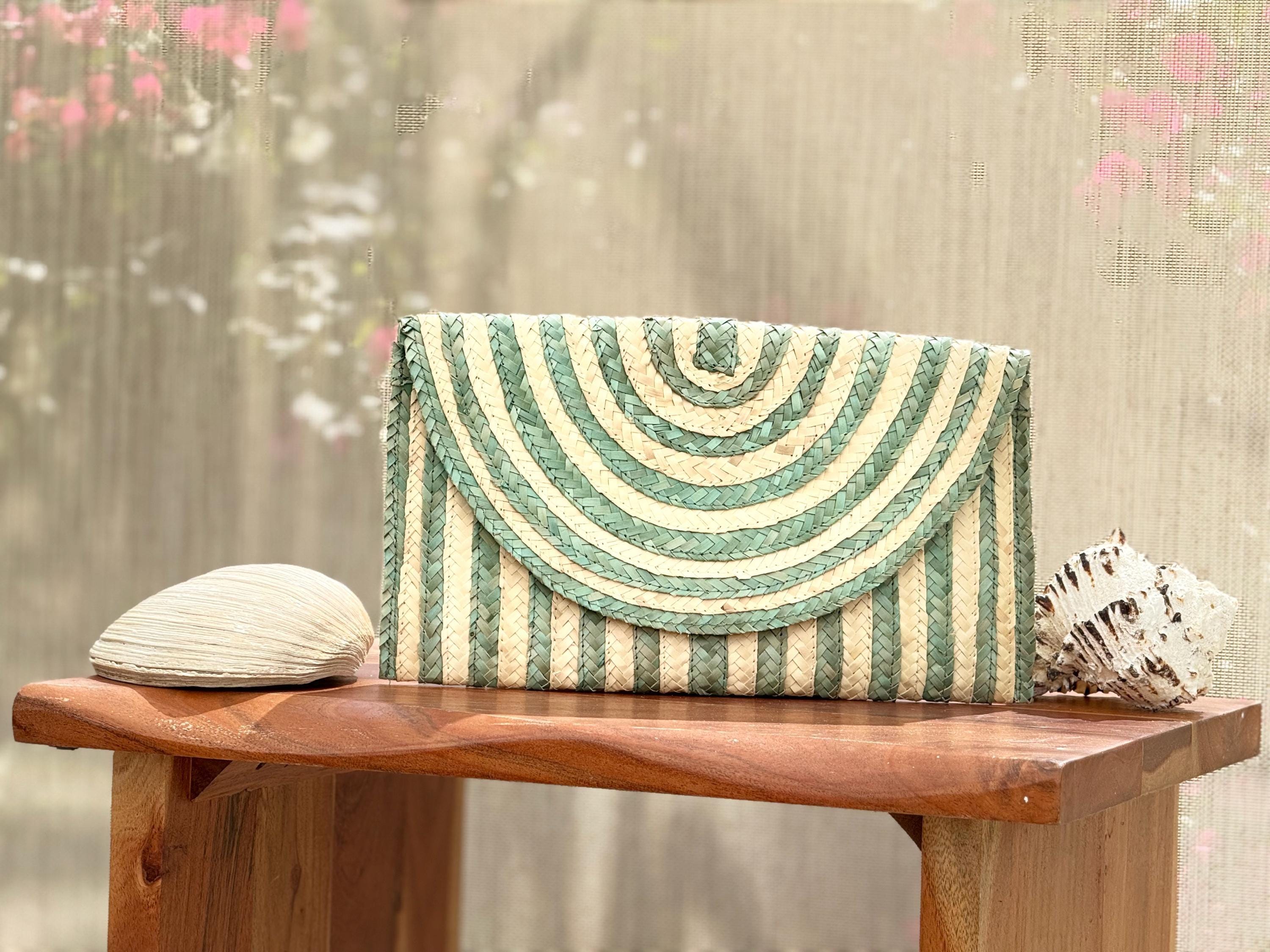 A striped purse with a green and white pattern sits on a wooden table, accompanied by a seashell and a small white object.