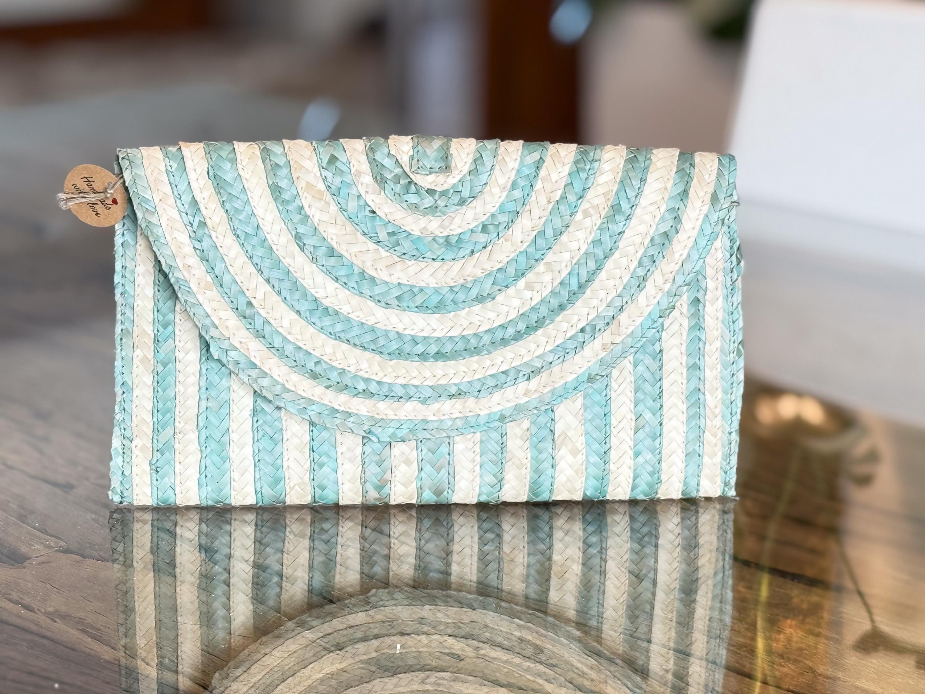 A light blue and white striped clutch purse is displayed on a reflective surface, with a tag attached to it.