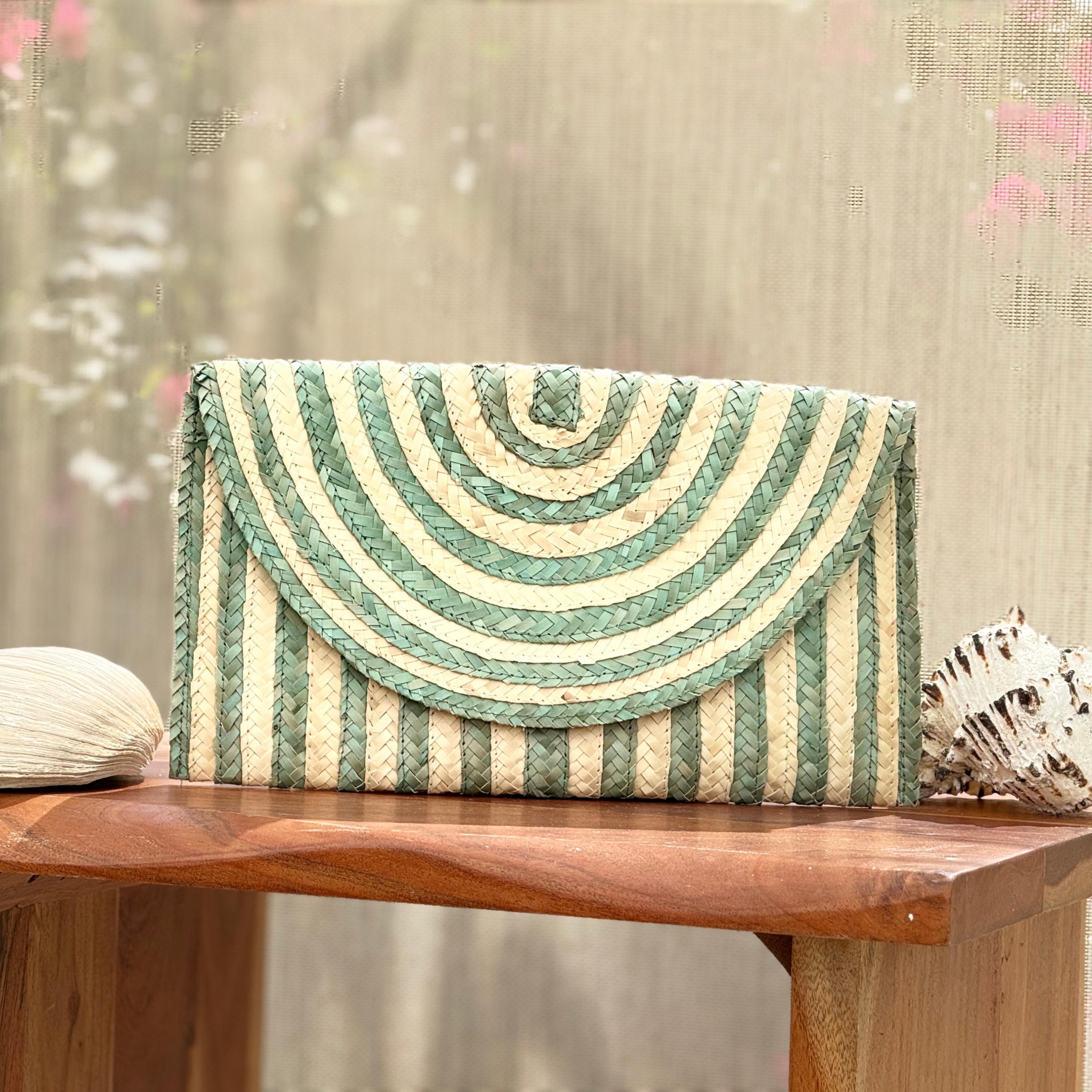 A striped purse with a green and white pattern sits on a wooden table, accompanied by a seashell.
