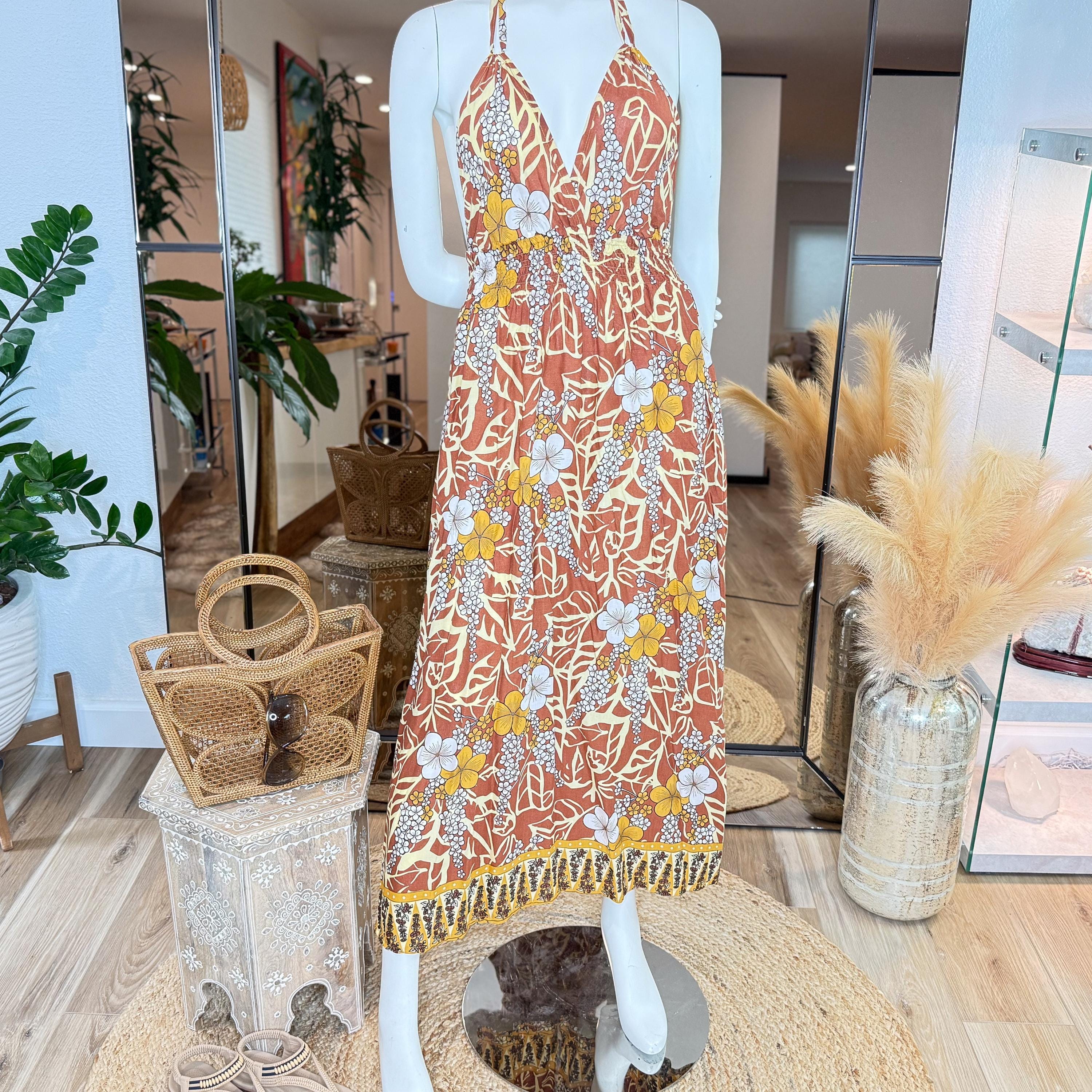 A mannequin wearing a vibrant floral print dress stands in a room with various decorative elements, including potted plants and a woven basket.