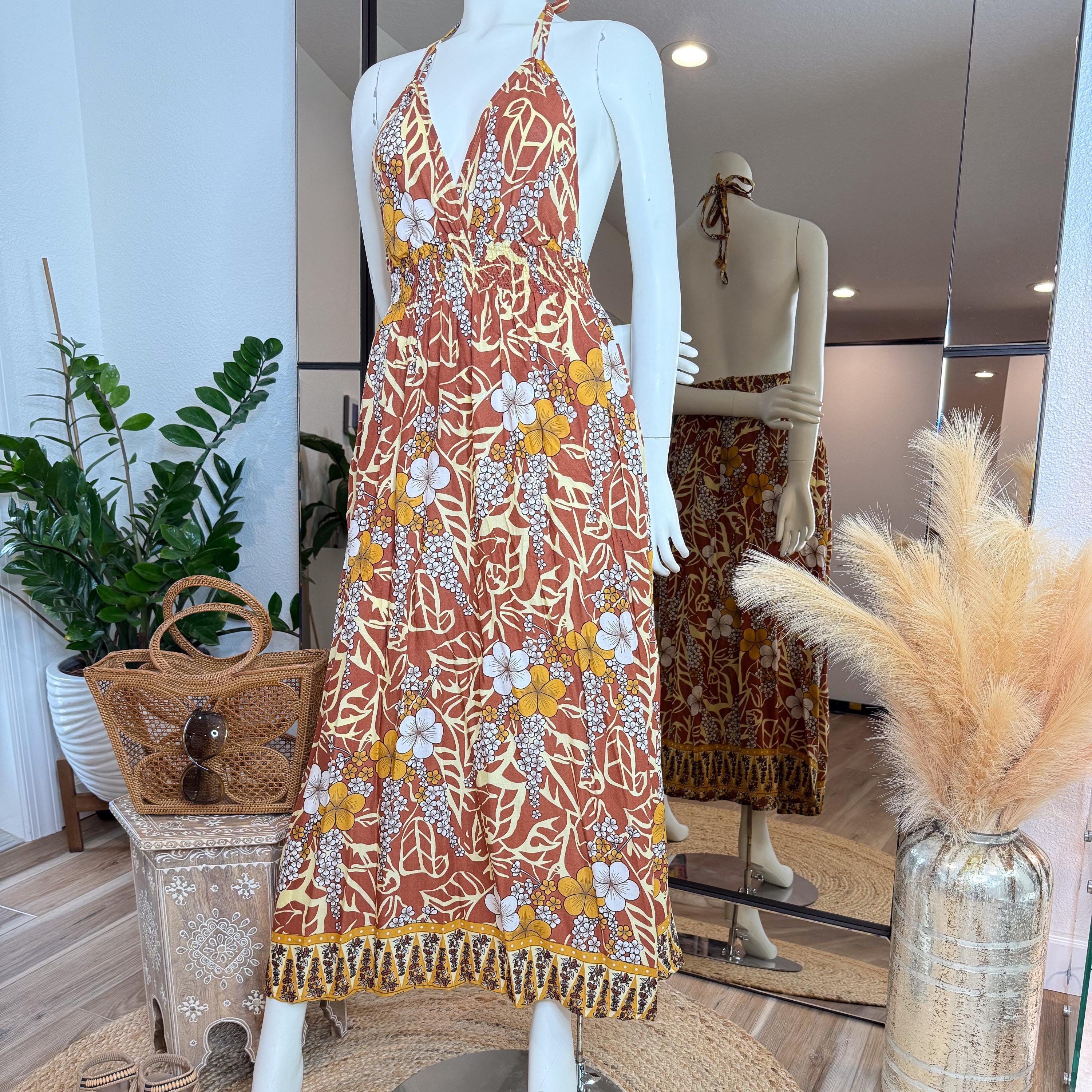 A mannequin wearing a floral print dress stands in a clothing store, with a handbag and potted plants visible in the background.