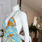 A mannequin wearing a blue and orange floral dress with a halter neckline and a tie at the neck.