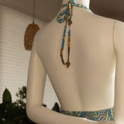 the back view of a mannequin wearing a colorful dress with a patterned neckline and a blue and yellow tie.