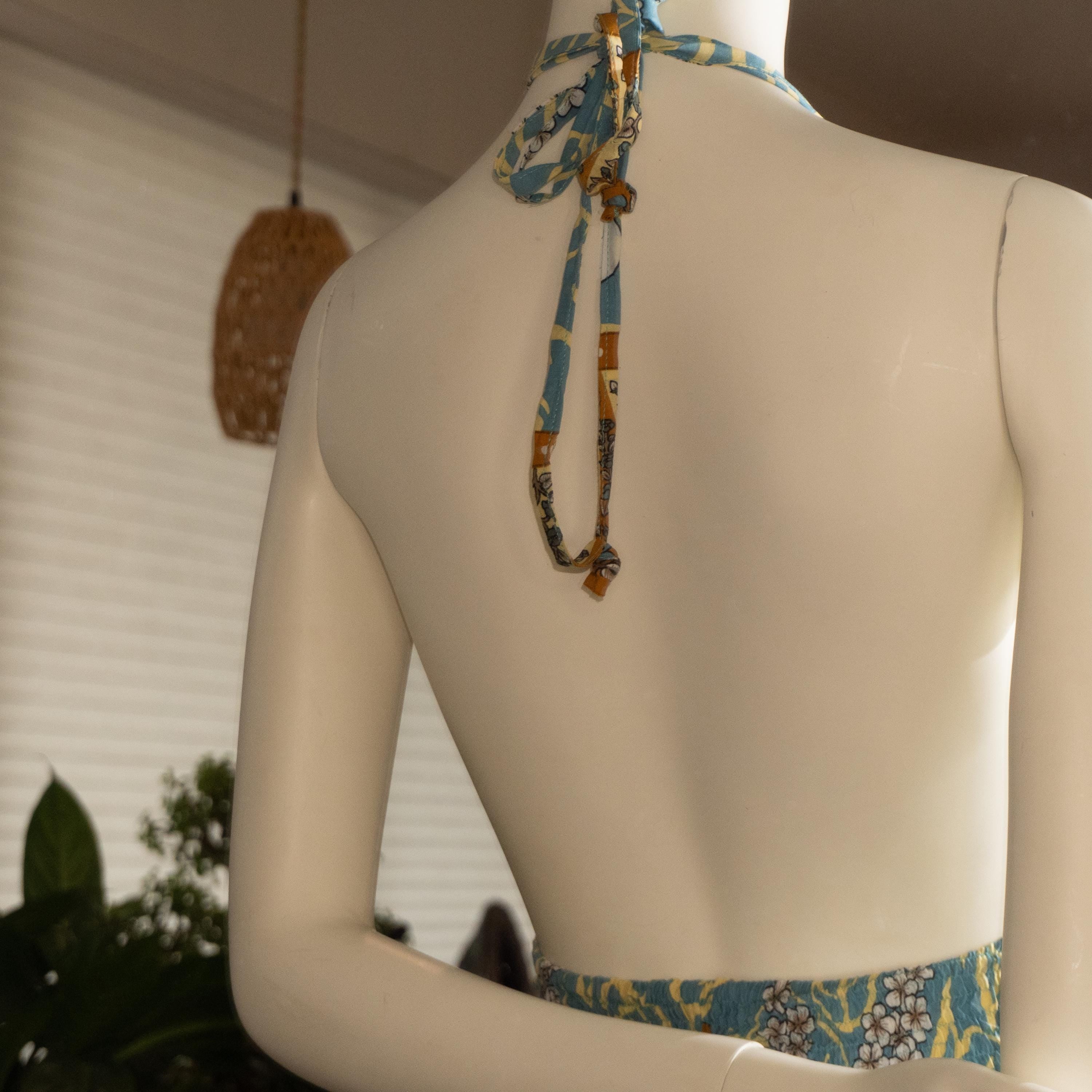 the back view of a mannequin wearing a colorful dress with a patterned neckline and a blue and yellow tie.