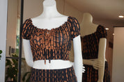 A mannequin wearing a black and orange patterned dress with a ruffled neckline and short sleeves, displayed in a store window.