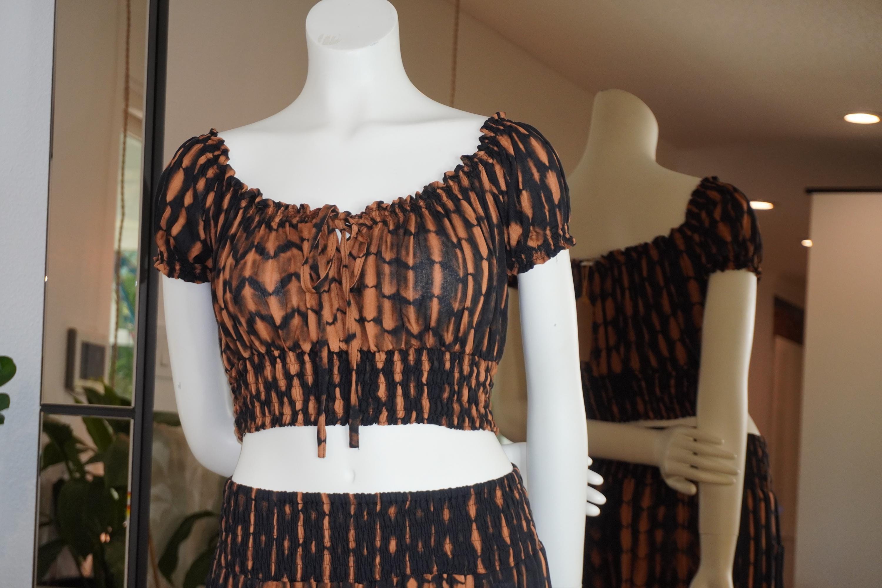 A mannequin wearing a black and orange patterned dress with a ruffled neckline and short sleeves, displayed in a store window.