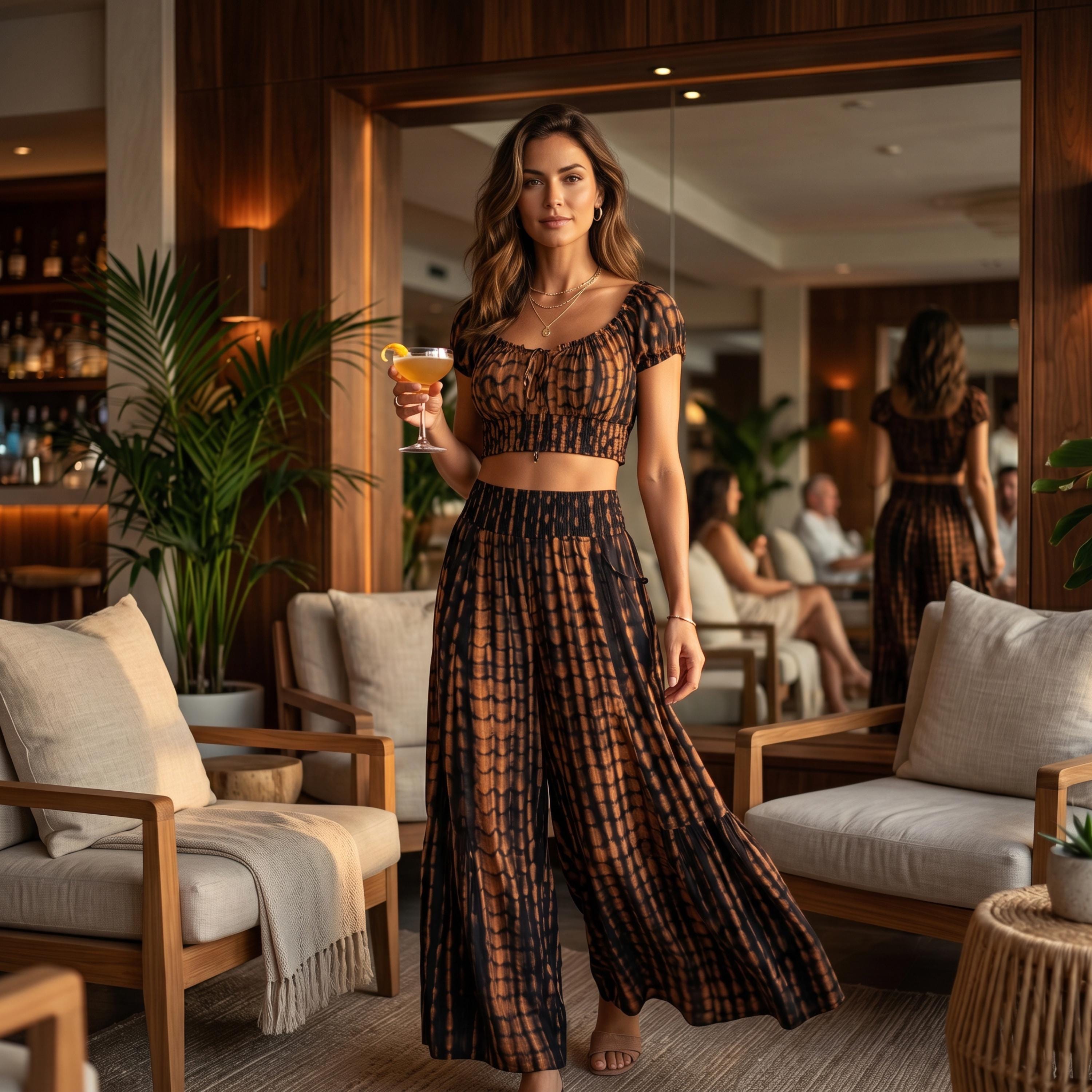 A woman in a black and orange patterned dress stands in a room with a mirror, holding a drink and surrounded by furniture.