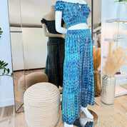 A mannequin wearing a blue patterned dress and matching skirt is displayed in a clothing store, with a mirror and decorative elements in the background.