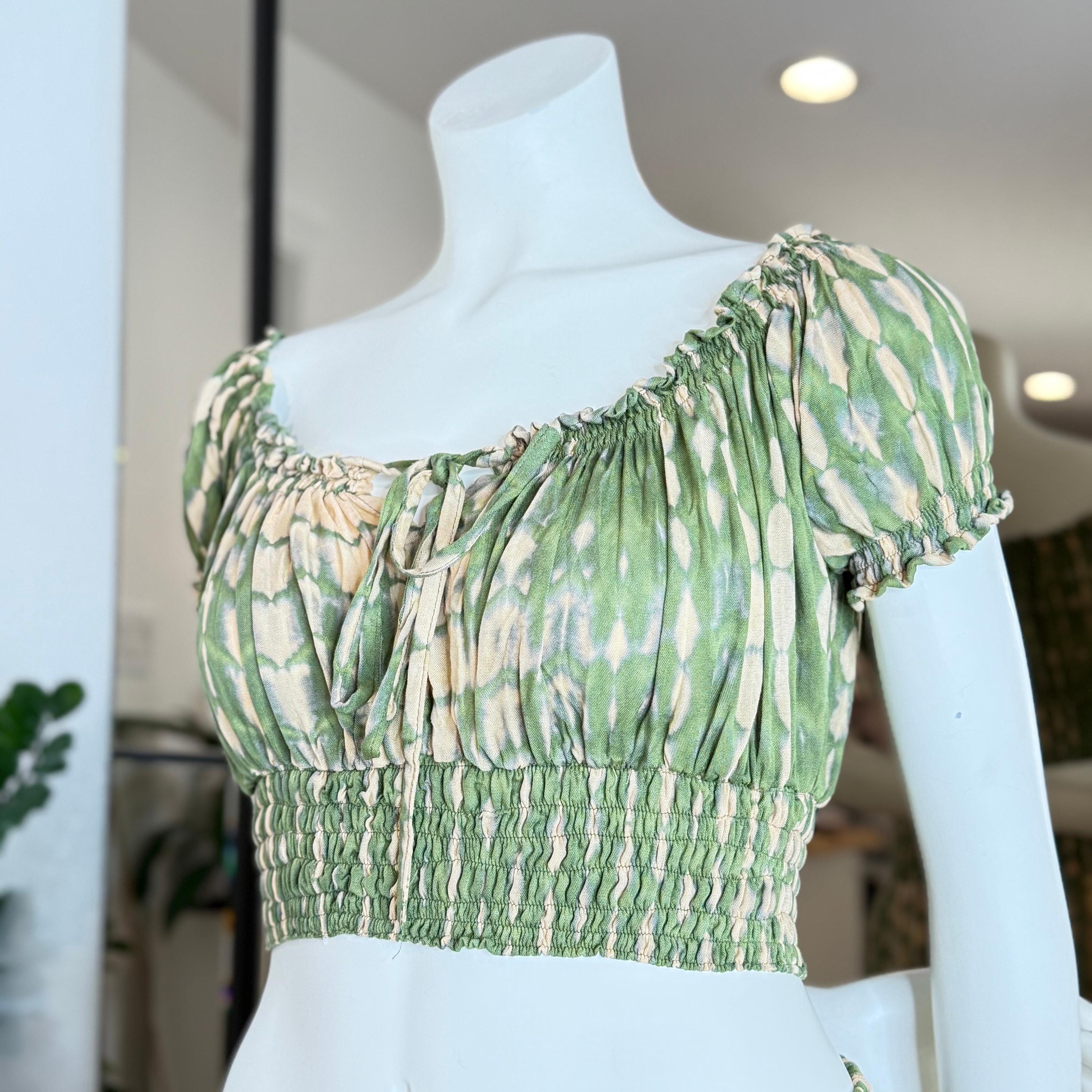 A mannequin wearing a green and white tie-dye crop top with a ruffled collar and a high-waisted design.