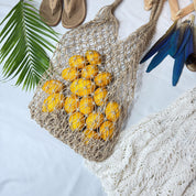 A woven mesh bag filled with bright yellow lemons, a pair of brown flip-flops, and a white lace garment are arranged on a white surface.