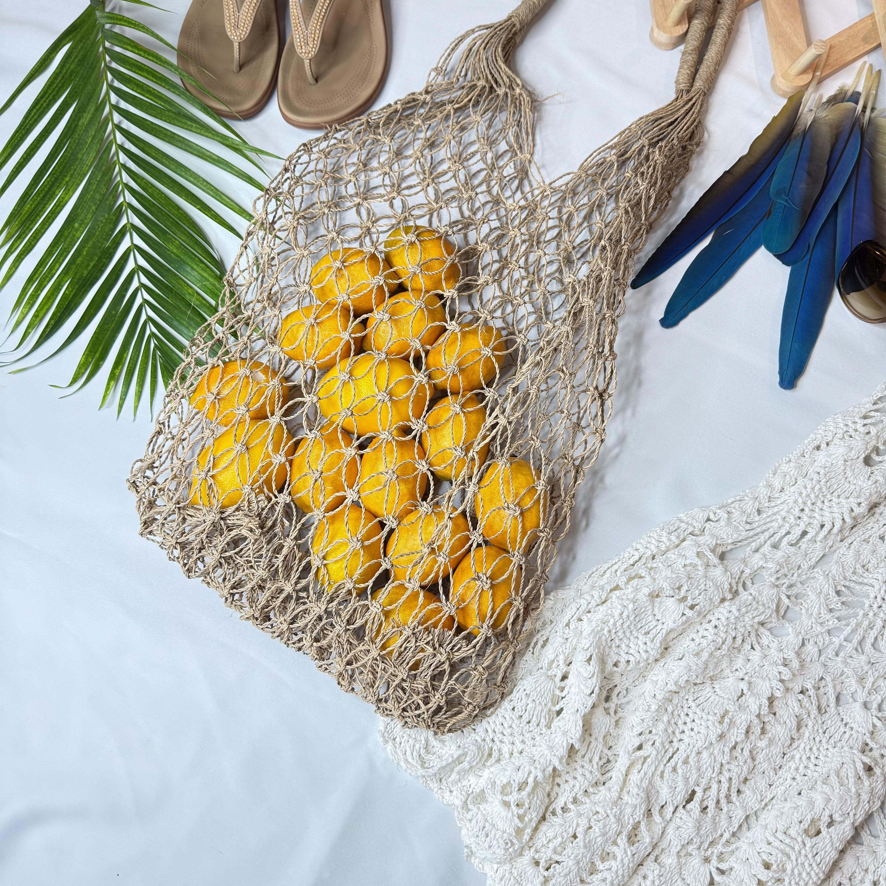 A woven mesh bag filled with bright yellow lemons, a pair of brown flip-flops, and a white lace garment are arranged on a white surface.