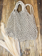 A beige mesh bag with handles is placed on a wooden surface, accompanied by a piece of white material.