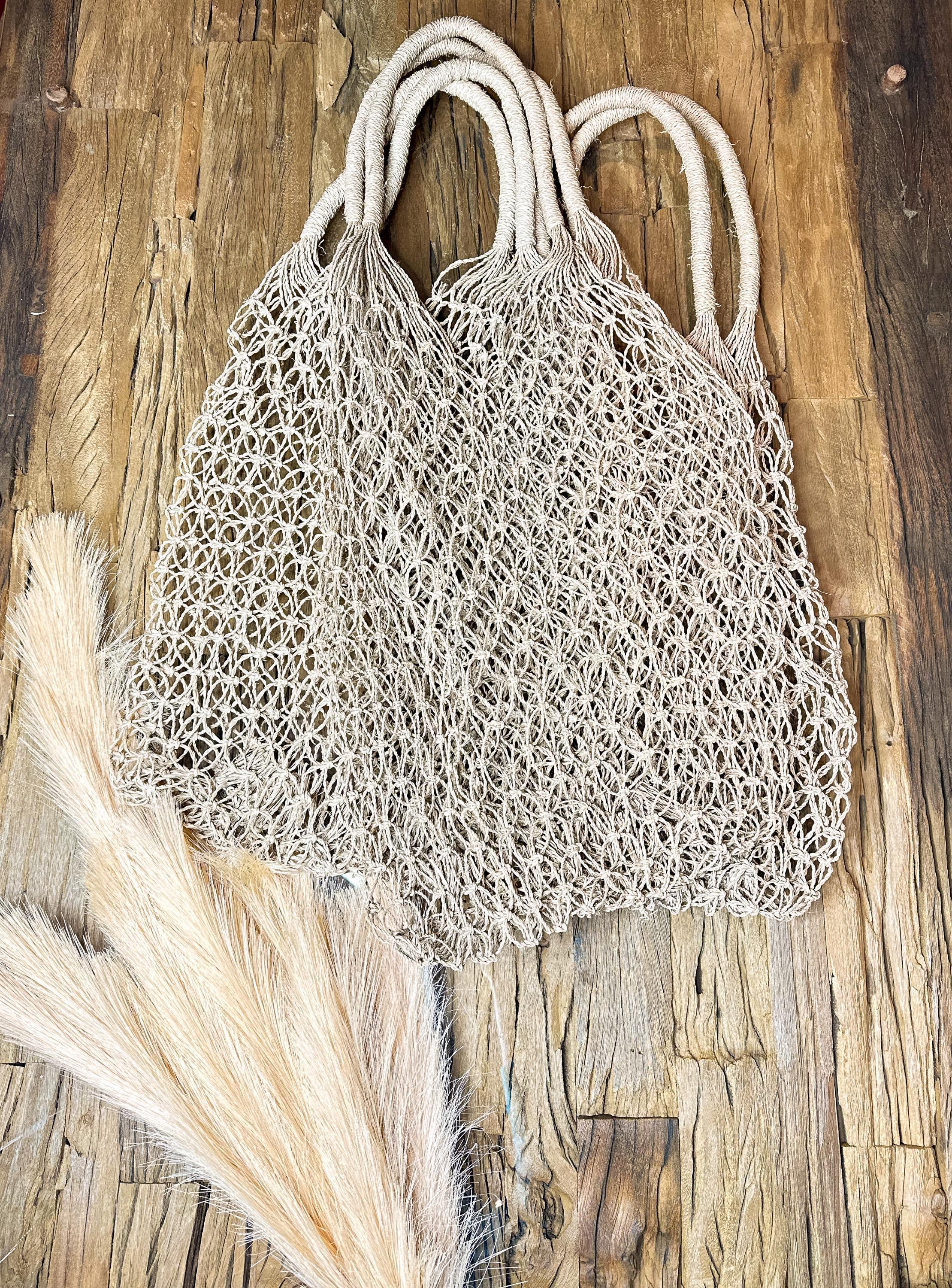A beige mesh bag with handles is placed on a wooden surface, accompanied by a piece of white material.