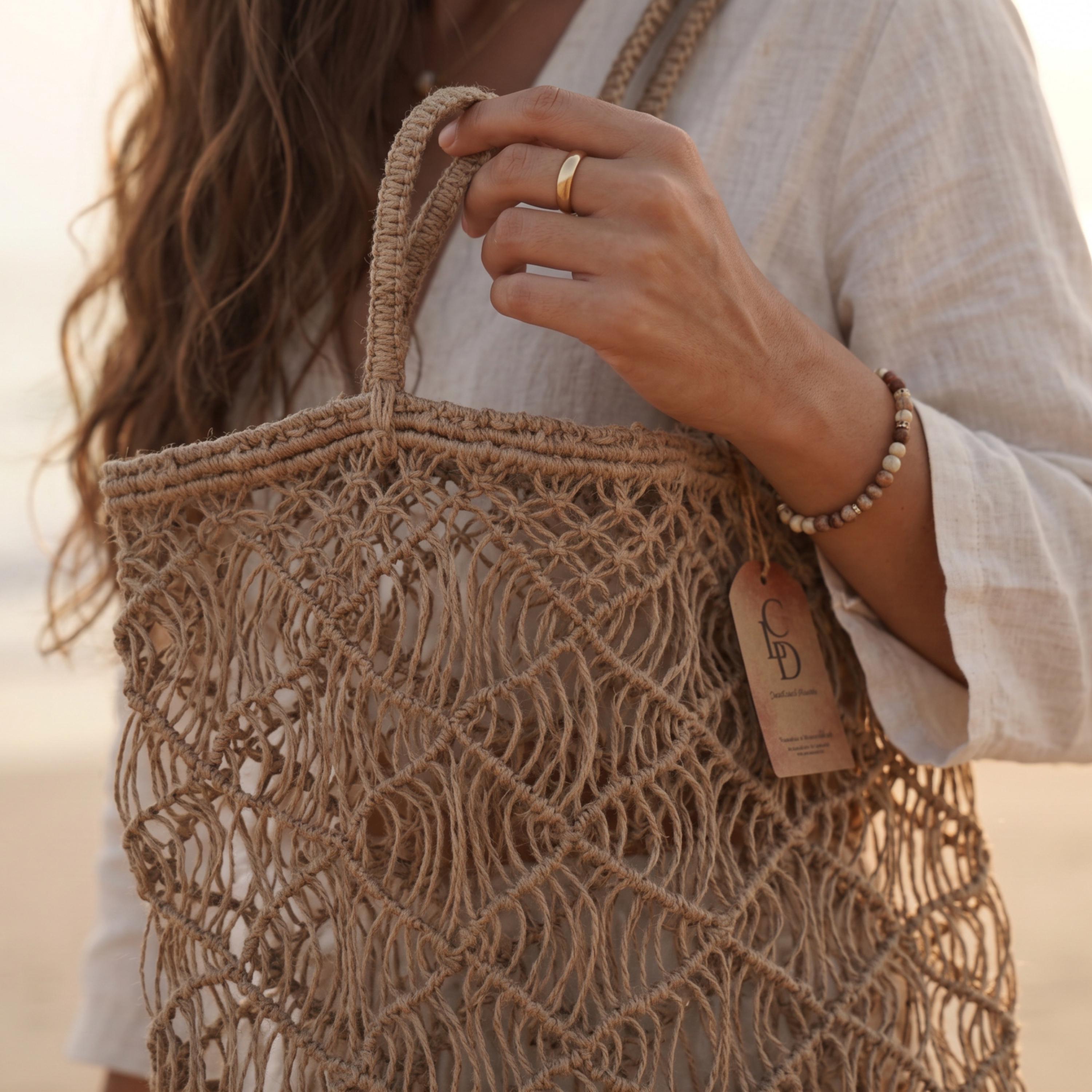 A close-up of a hand holding a woven straw bag with a tag attached.