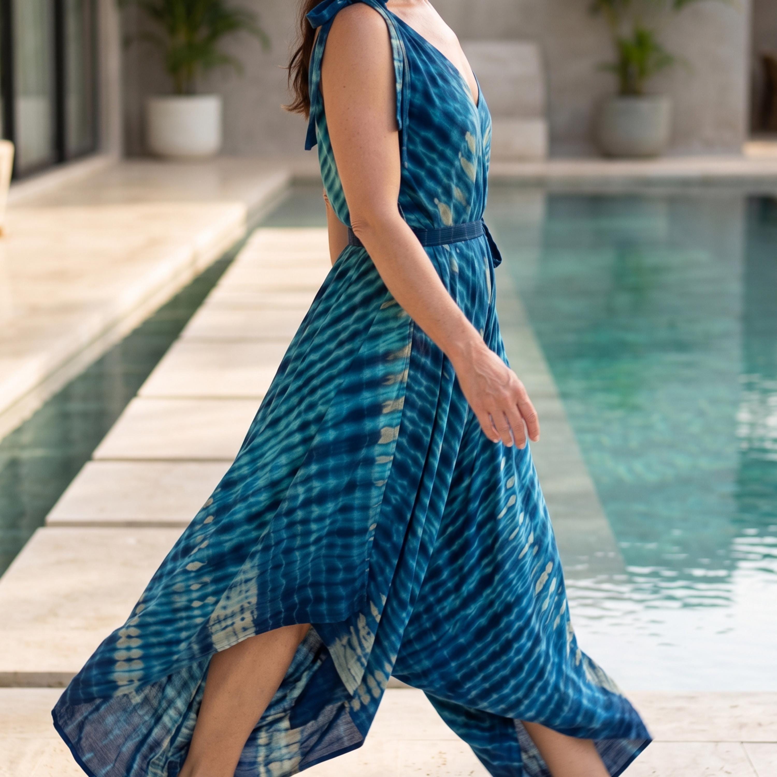 A woman wearing a blue and white tie-dye dress is walking near a pool.