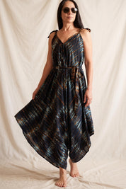 A woman wearing a black and blue tie-dye jumpsuit with a high neckline and a belt, posing against a beige background.