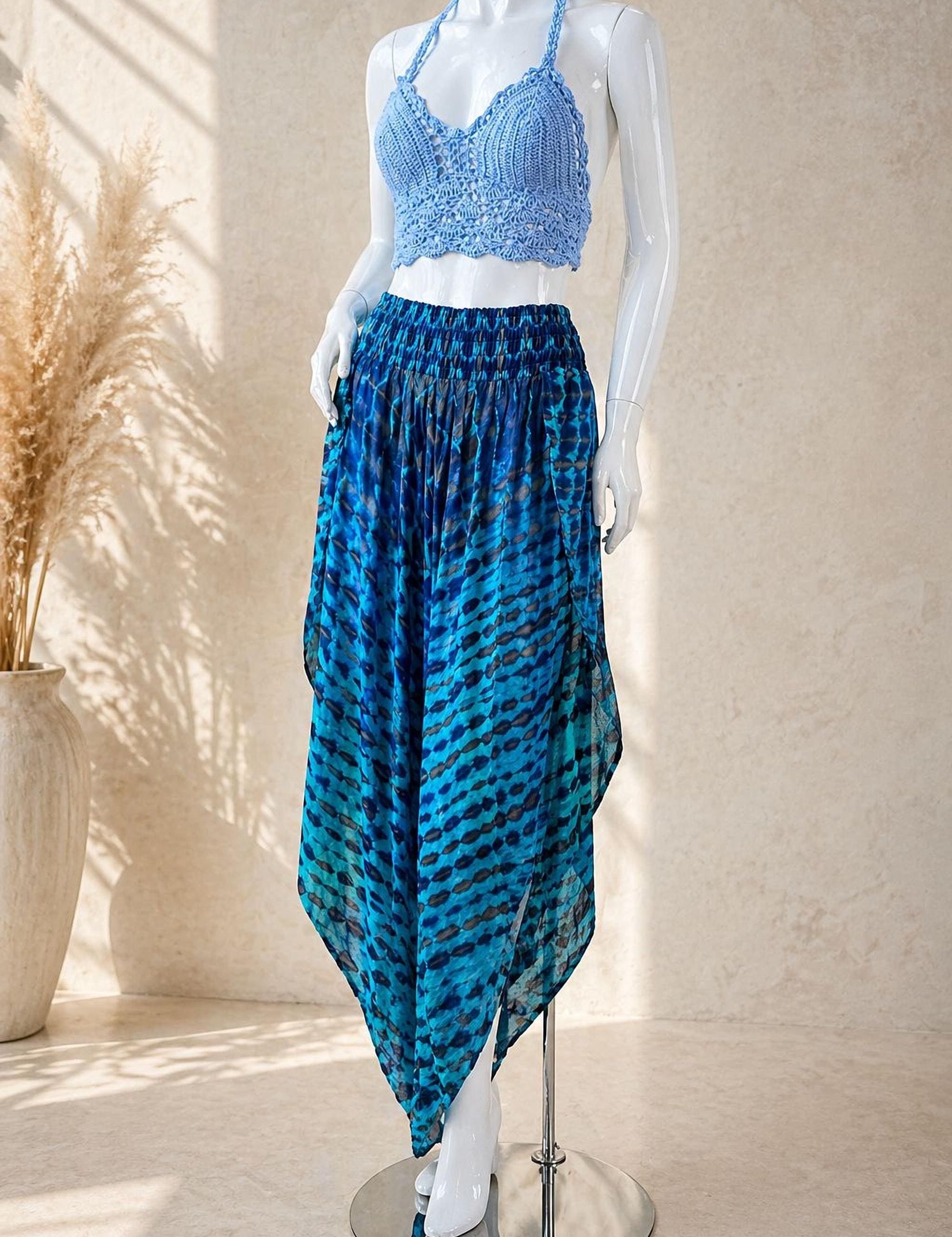 A mannequin wearing a blue crocheted top and a blue and black patterned skirt, standing on a silver stand against a beige wall.