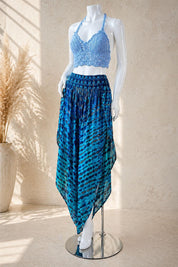 A mannequin wearing a blue crocheted top and a blue and black patterned skirt, standing on a silver stand against a beige wall.