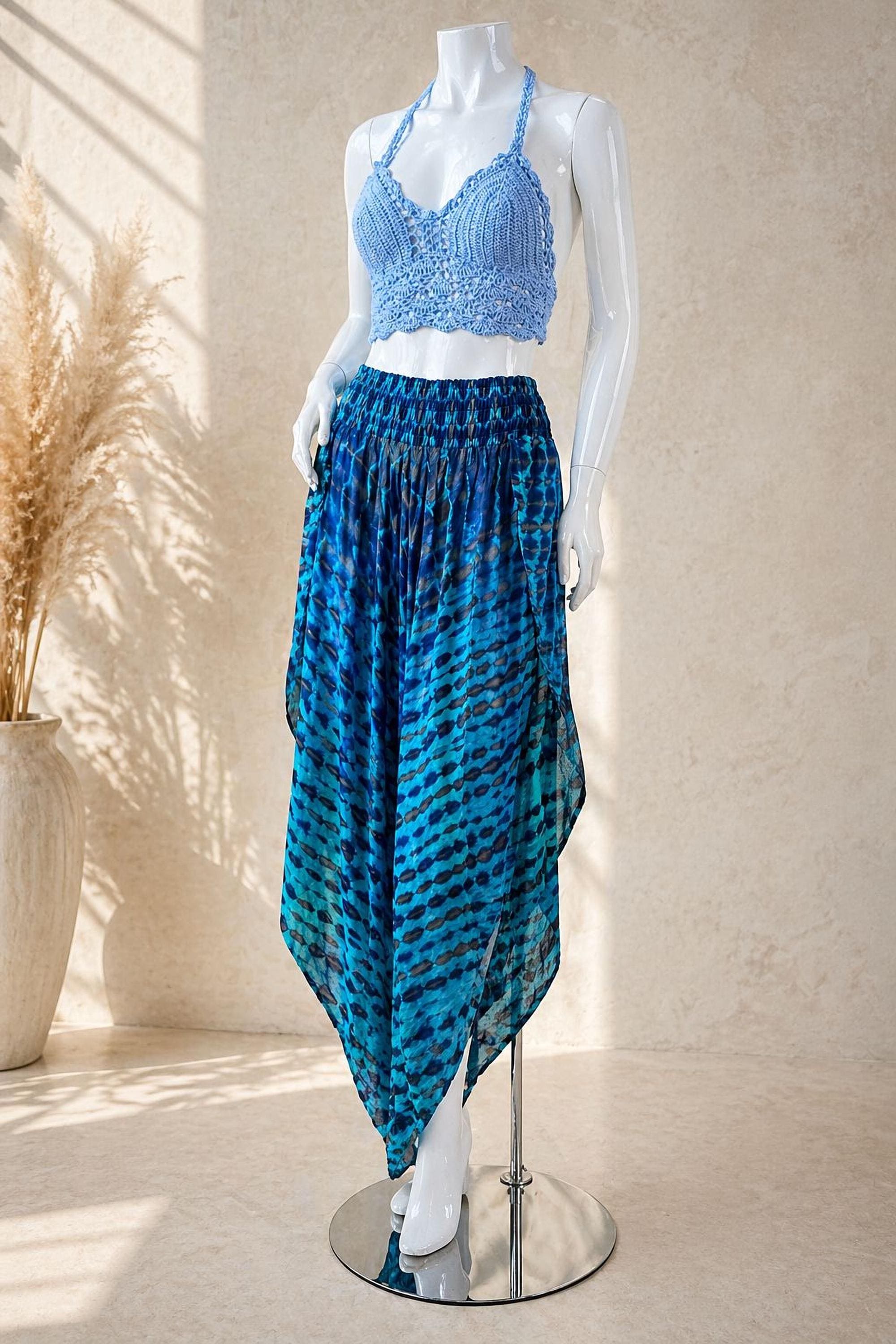 A mannequin wearing a blue crocheted top and a blue and black patterned skirt, standing on a silver stand against a beige wall.