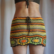 A person wearing a colorful, crocheted skirt with a pattern of orange, green, and yellow stripes.