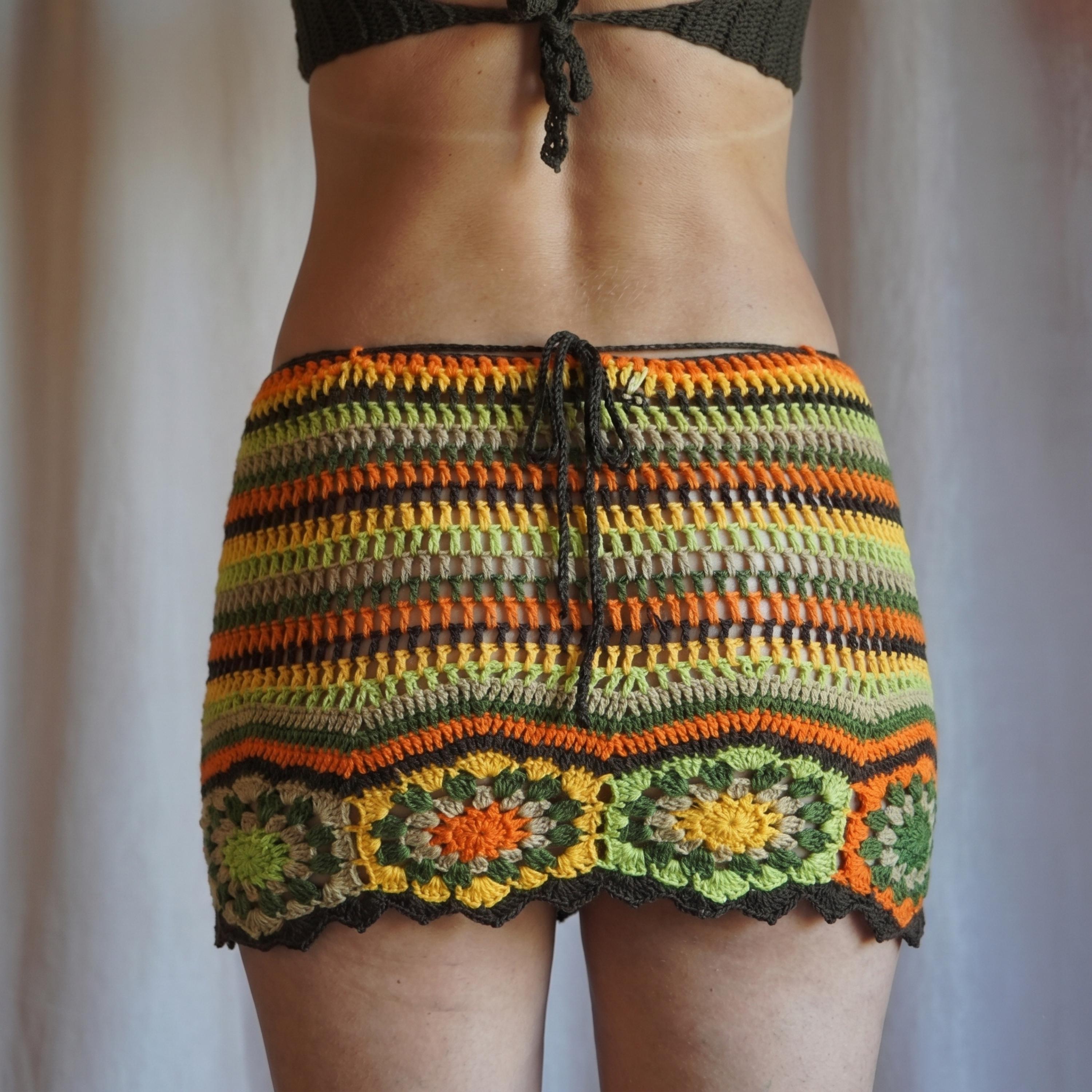 A person wearing a colorful, crocheted skirt with a pattern of orange, green, and yellow stripes.