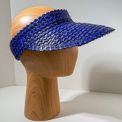 A wooden mannequin head wearing a blue woven visor.