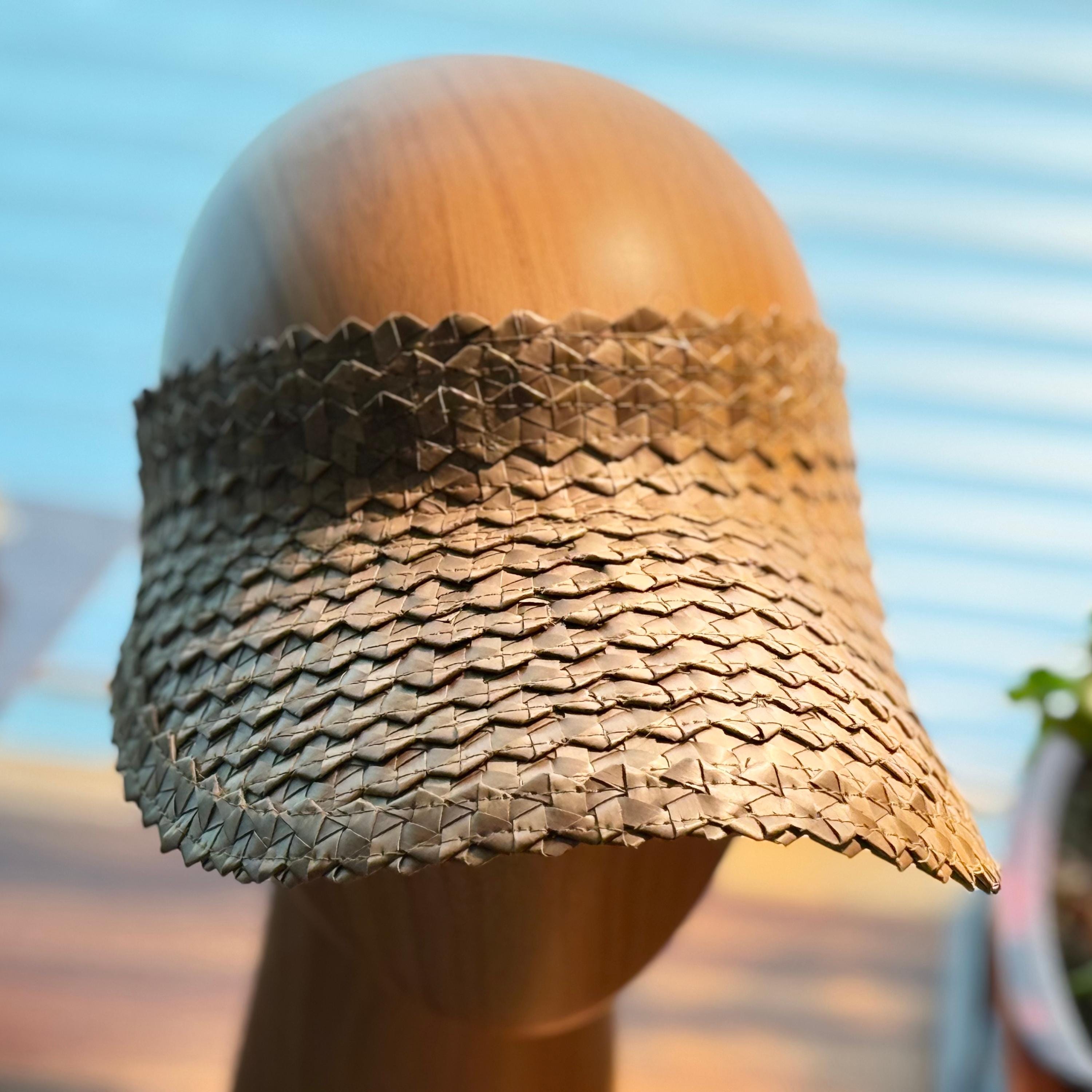 A wooden headless mannequin head wearing a woven straw hat with a textured pattern.