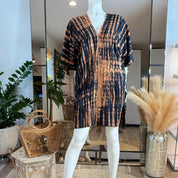 A mannequin wearing a tie-dye dress with a black and orange pattern, placed in a room with potted plants and a mirror.