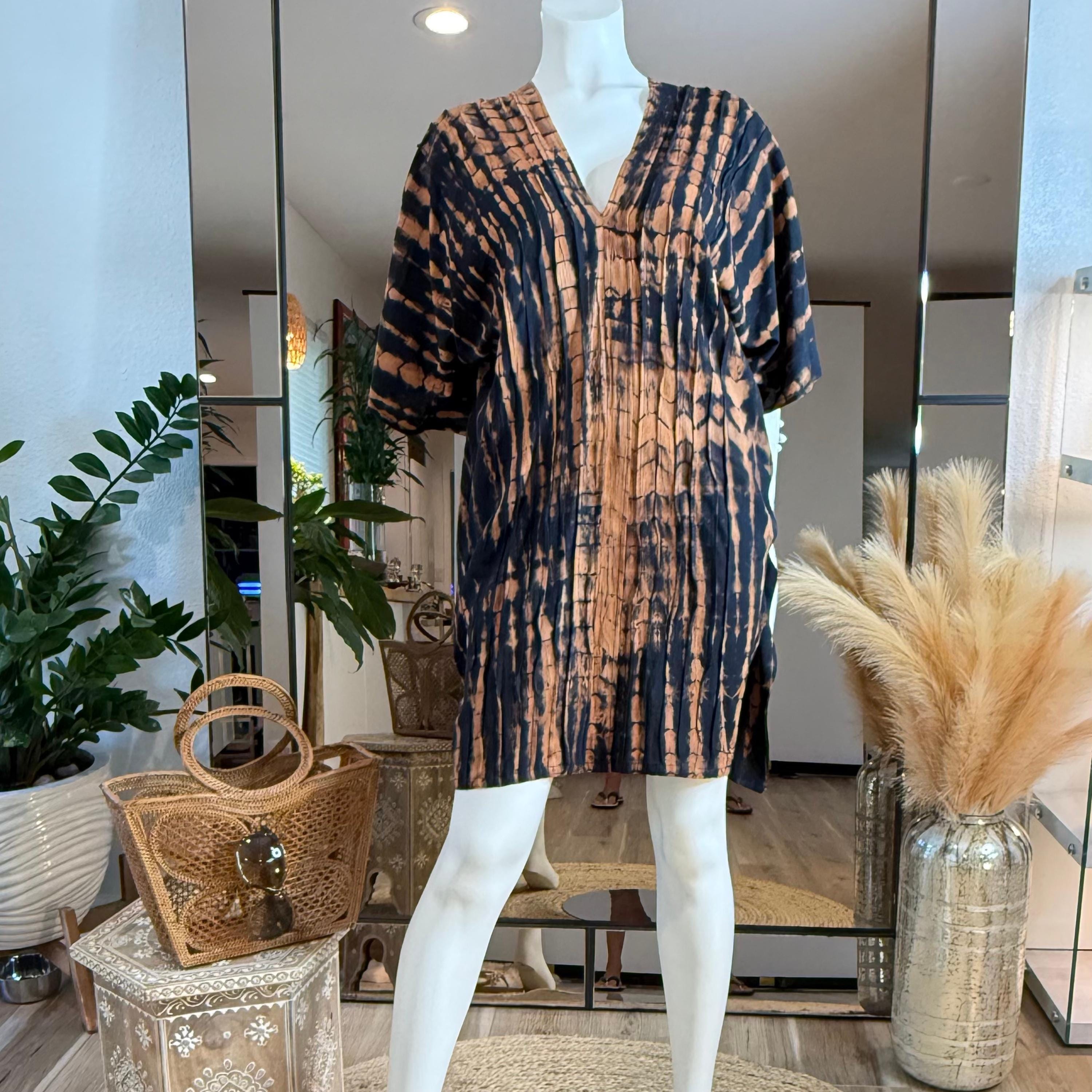 A mannequin wearing a tie-dye dress with a black and orange pattern, placed in a room with potted plants and a mirror.
