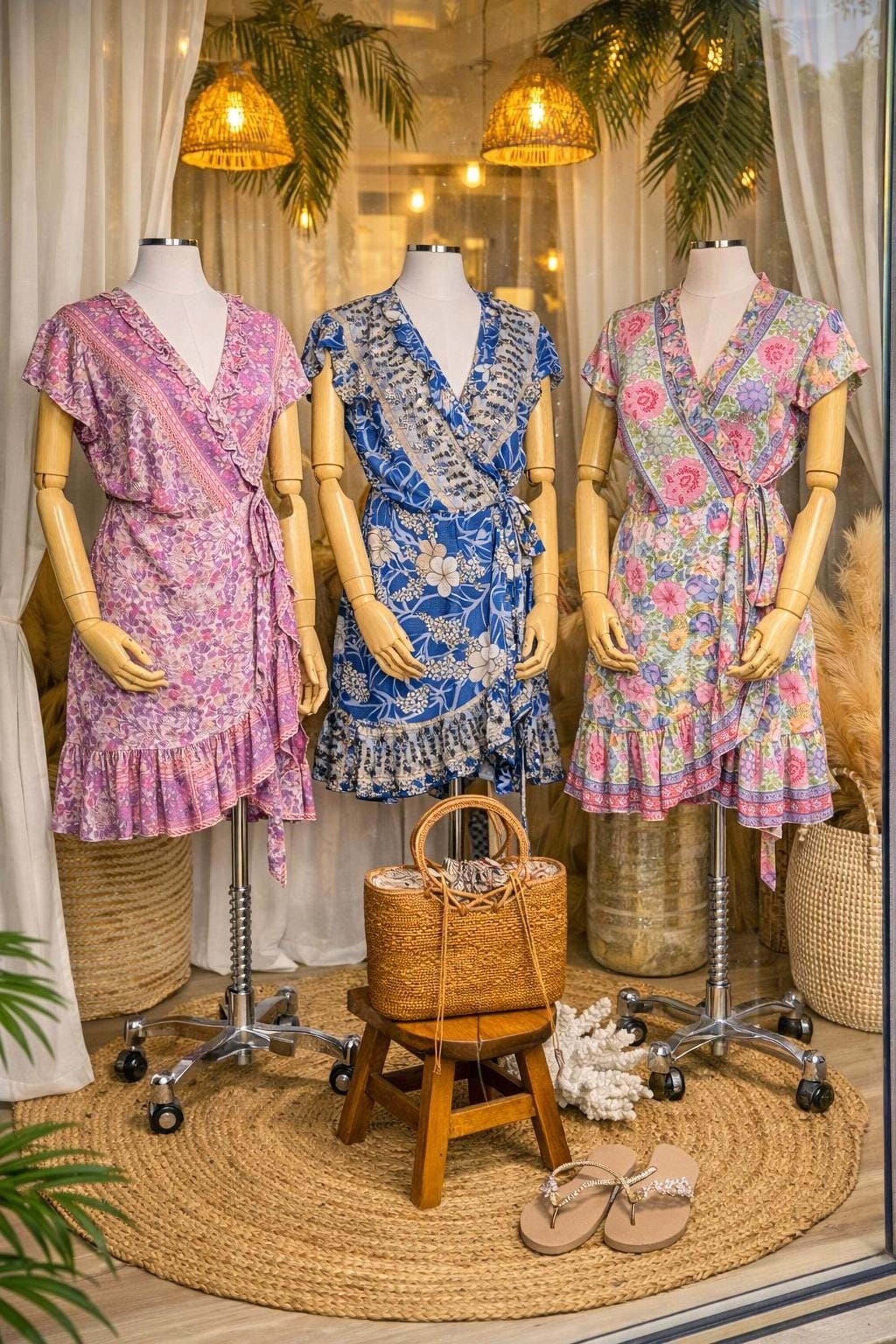 A display of three colorful dresses on mannequins, with a woven basket and a pair of sandals in the foreground.