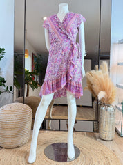 A mannequin wearing a purple floral wrap dress with a ruffled hem and a tie at the waist, displayed in a clothing store.