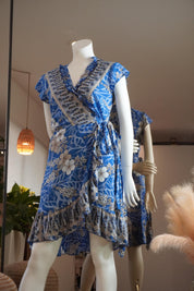 A mannequin wearing a blue wrap dress with a floral pattern and frills, displayed in a store.